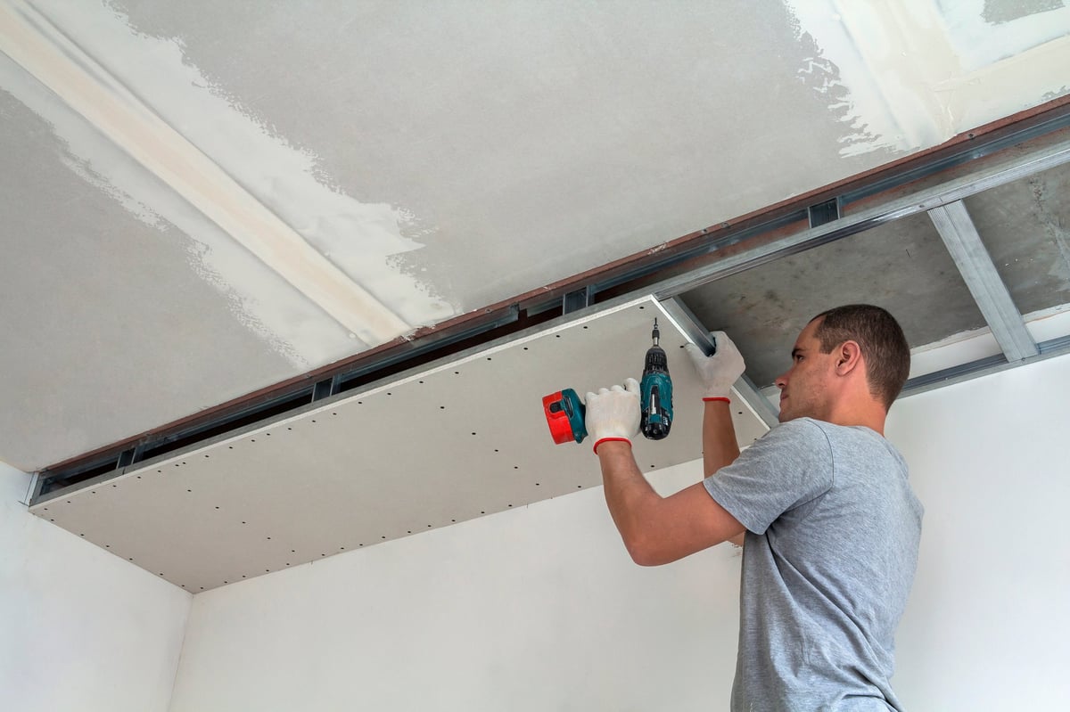 Worker fixing drywall to a metal frame ceiling